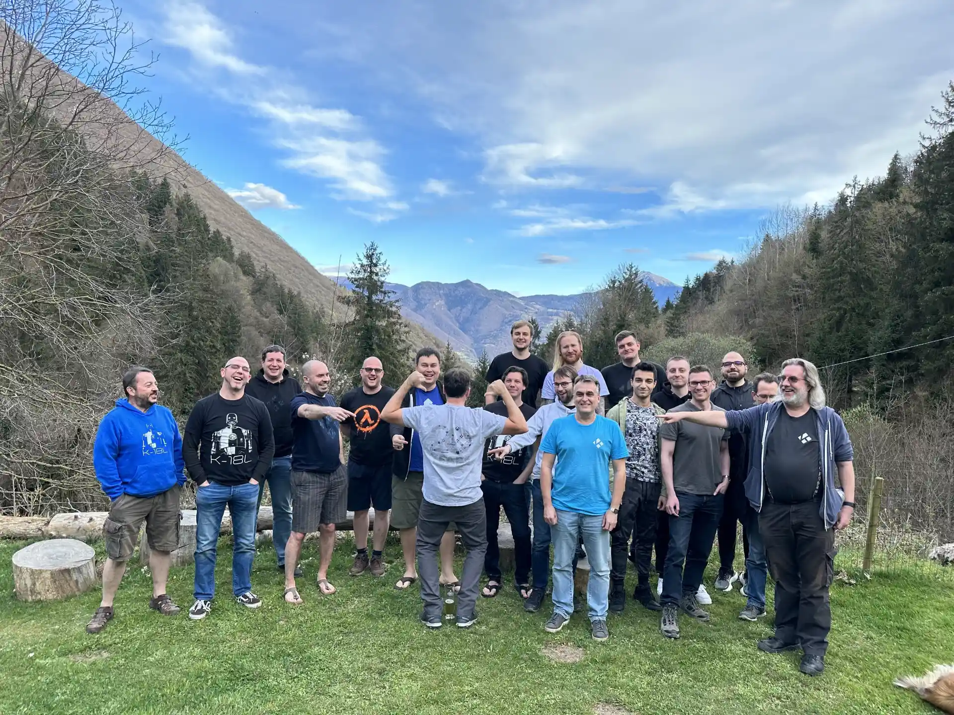 Team Kodi, 2023 - Italy Team Kodi, 2023 - Kodi team members at Devcon 2023. in northern Italy. A group of people stand, spread out, facing the camera. Grass in front, but mountains soar in the background behind this motley crew of technological reprobates. One team member has his back turned to the camera, while people point to the logo on the back of his shirt: the numbers 20, signifying the 20th anniversary of XBMC/Kodi, but made up of the names of all the people and companies that have helped us make this awesome software happen.